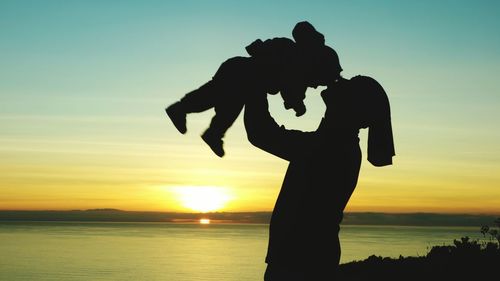 Silhouette father carrying kid against sky during sunset