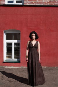 Beautiful woman in brown dress standing against red wall