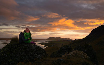 Woman sitting on rock against sky during sunset