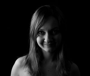 Close-up portrait of smiling young woman against black background