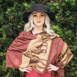 Portrait of woman wearing scarf and hat standing with hands on hip against plants