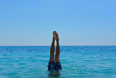 Low section of man in sea against clear sky