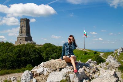 Full length of young woman sitting on rocks against monument of freedom