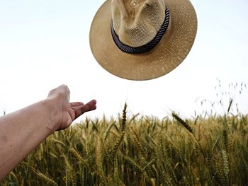Cropped image of person throwing sun hat over wheat field against sky