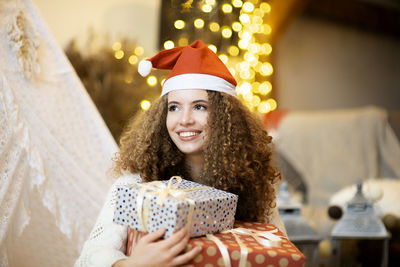 Pretty woman holding  christmas giftboxes wear knitted pullover and santa hat on bokeh  background