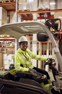 Portrait of smiling young female worker driving forklift in industry