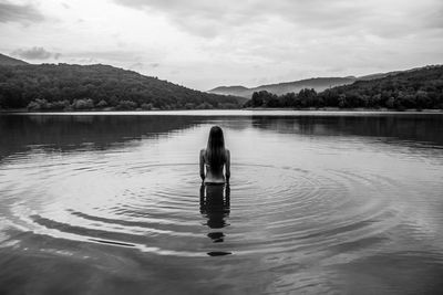 Rear view of woman standing in lake against cloudy sky