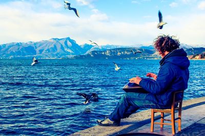 Rear view of woman sitting on chair by sea against sky