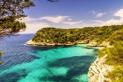 Scenic view of sea and tree covered rocky mountains at cala mitjana