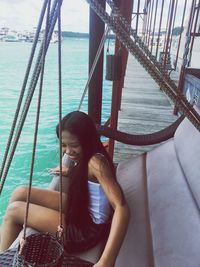 Side view of young woman sitting by lake on swing at pier