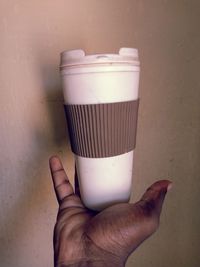 Close-up of hand holding drink against wall