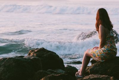 Woman wearing dress sitting on rock against sea