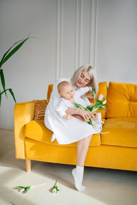 Mother with child in white clothes on a yellow sofa bouquet of flowers tulips spring