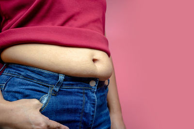 Midsection of woman standing against pink background