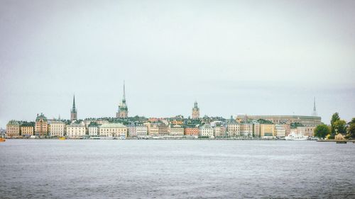 View of buildings by river in city against sky