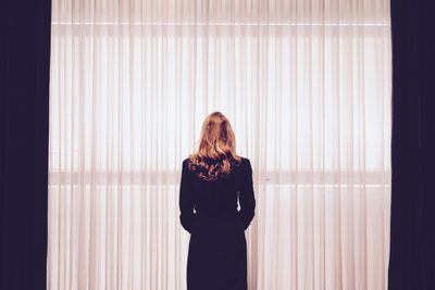 Rear view of woman with brown hair standing in front of curtain