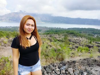 Portrait of beautiful young woman standing on mountain against sky