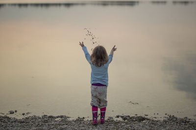 Rear view of girl throwing stones in lake at beach