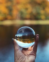 Cropped hand of woman holding crystal ball against lake