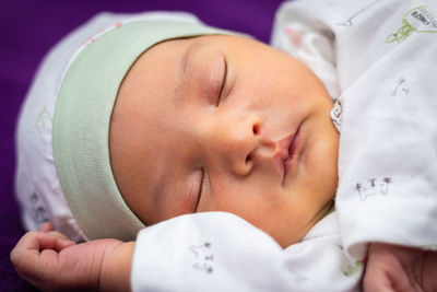 Newborn baby isolated sleeping in white cloth with purple background from different angle