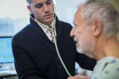 Male doctor listening to patient's breathing in hospital ward