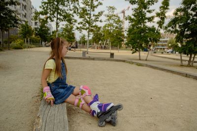 Side view of girl with inline skates sitting in park
