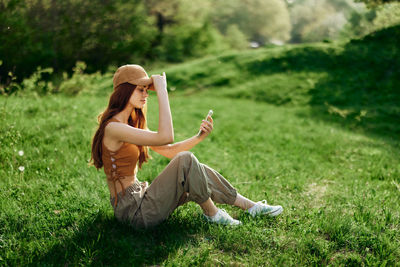 Rear view of young woman using mobile phone while sitting on grassy field