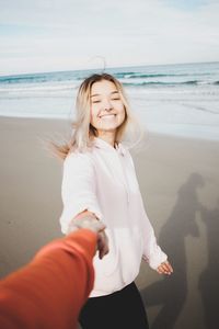 Cropped image of man holding happy woman hand at beach