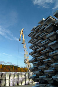 Stack of metals with crane in background against sky