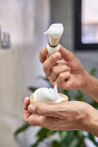 Hands of man holding shaving cream and brush in bathroom at home