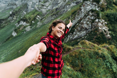 A young happy woman holds the hand of a partner in the mountains, offering to follow her.