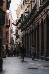 Rear view of people walking on street amidst buildings in city