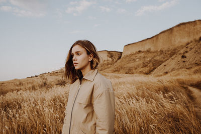 Young woman standing on field against sky