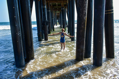 Rear view of woman standing below pier at beach