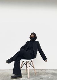 Full length of young woman sitting on chair against wall