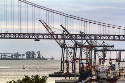 Cranes on bridge over river against sky