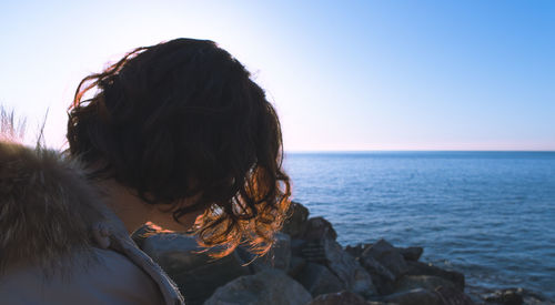 Rear view of girl standing by sea against clear sky