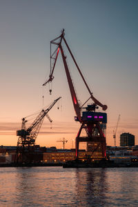 Cranes at commercial dock against sky during sunset