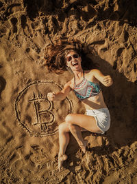 Full length of woman lying by bitcoin symbol at beach