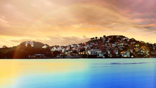 Buildings by sea against sky during sunset