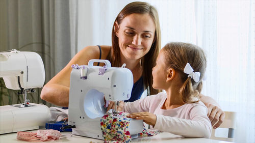 Smiling mother looking at daughter while sewing