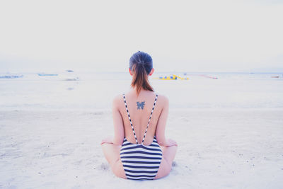 Rear view of woman standing on beach against clear sky