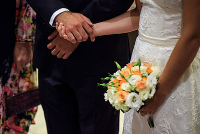 Midsection of newlywed couple holding hands at wedding ceremony