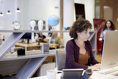 Senior businesswoman using desktop computer while sitting at desk in creative office