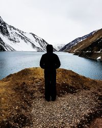 Rear view of man standing on snowcapped mountain against sky