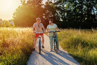 Happy smiling senior couple riding bicycles together outdoors in countryside at warm sunny day.