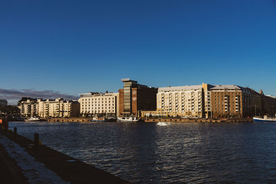 Buildings by sea against clear blue sky