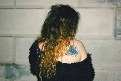 Rear view of woman with tattoo on back standing against wall