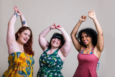 Portrait of smiling young women with arms raised against colored background