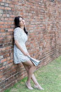 Side view of woman standing against brick wall